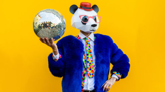 Brand Persona concept; man wearing a panda mask holding a disco ball on a yellow background