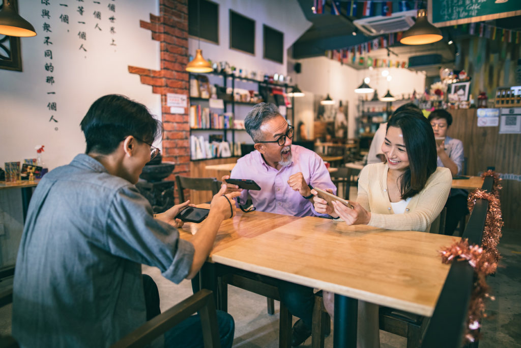 A group of 3 people sitting in a café playing their winning mobile game.