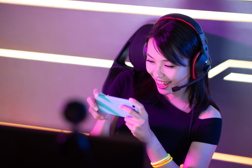A woman wearing a headphone happily playing her mobile game.